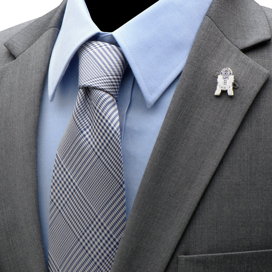 A silver-toned Star Wars R2-D2 Lapel Pin attached to the lapel of a gray suit jacket worn over a blue dress shirt and patterned tie.