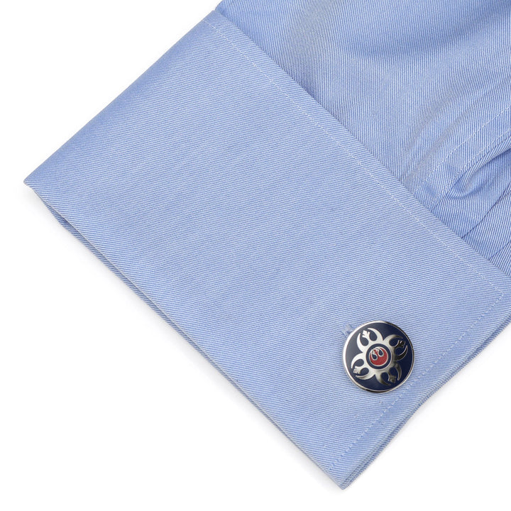 A blue dress shirt cuff fastened with a round Star Wars Rebel Alliance Starbird Crest Blue and Red Cufflink featuring a silver and red symbol on a dark blue background.