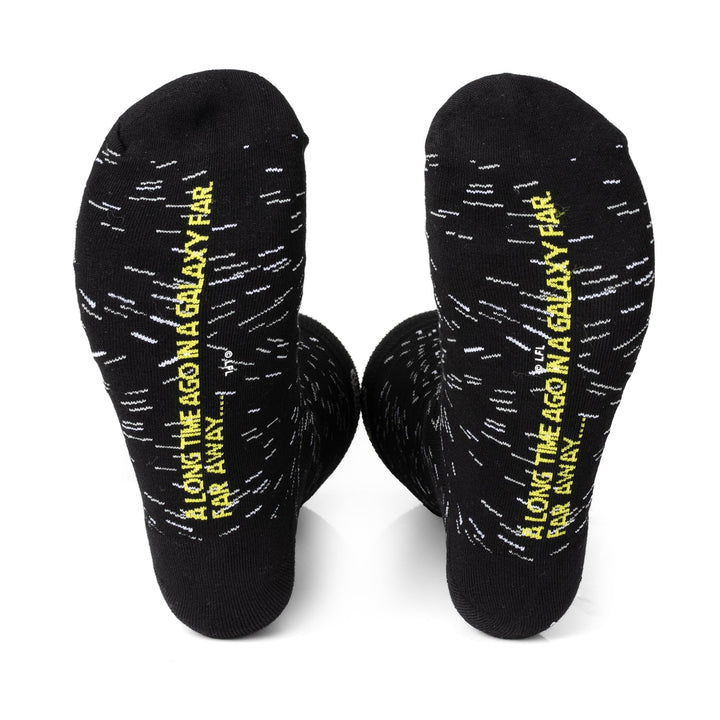 Two black Star Wars Transport 3 Pack Sock &amp; Lapel Pin Gift Set socks featuring white dashes and the yellow text “A long time ago in a galaxy far, far away...” printed on the soles.