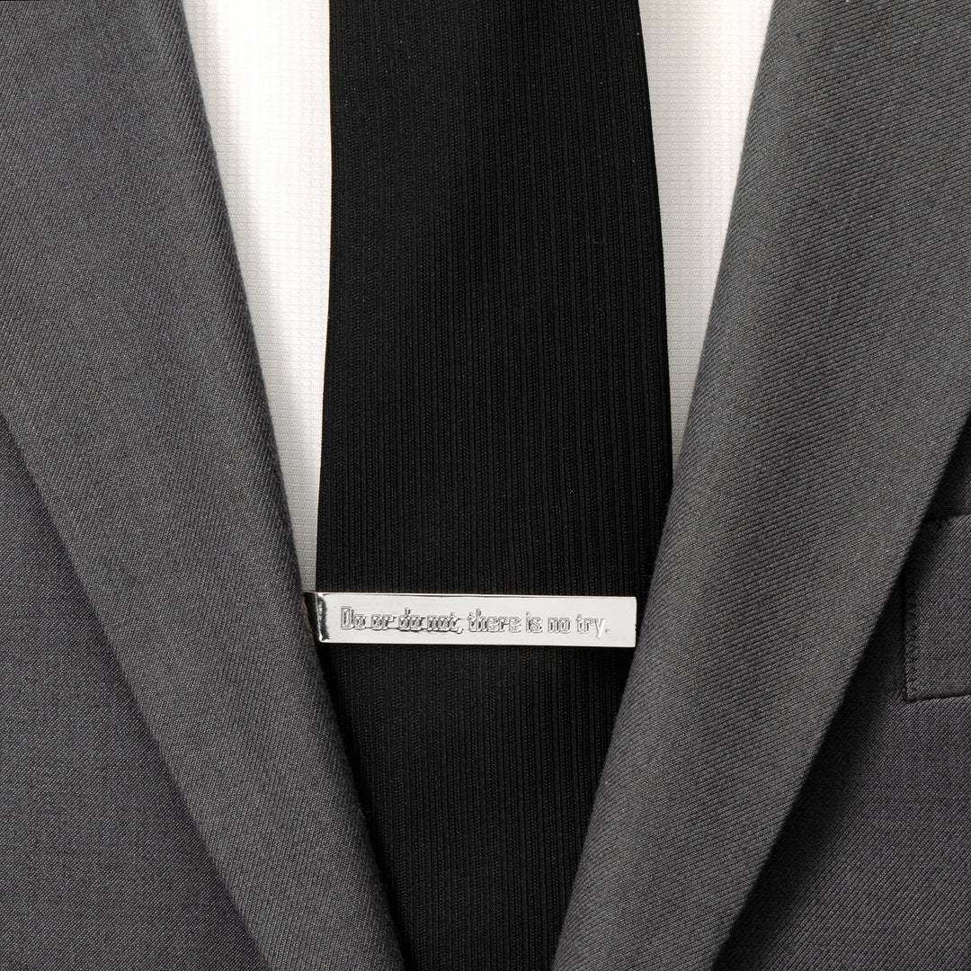 A silver Star Wars Yoda “There Is No Try” Tie Bar engraved with the words, “Do or do not, there is no try,” clipped to a black tie on a grey suit jacket.
