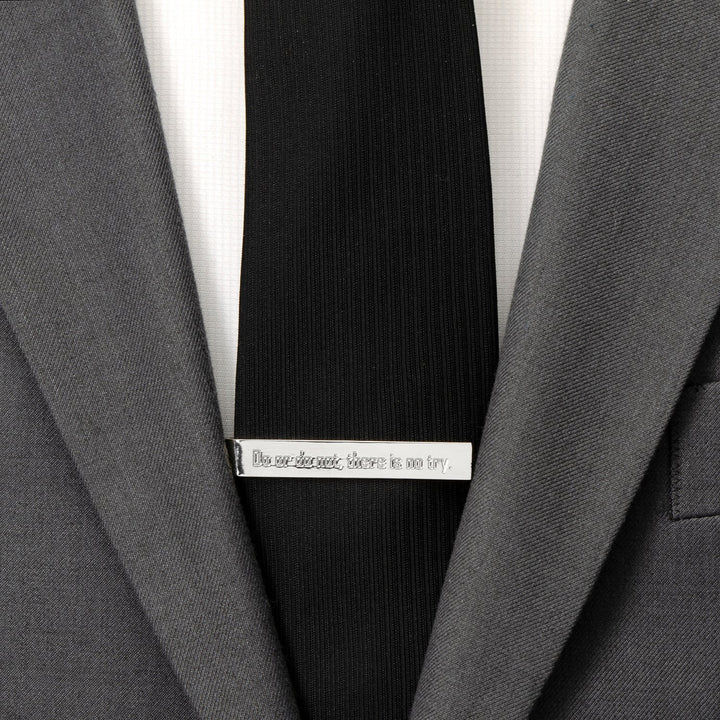 A silver Star Wars Yoda “There Is No Try” Tie Bar engraved with the words, “Do or do not, there is no try,” clipped to a black tie on a grey suit jacket.