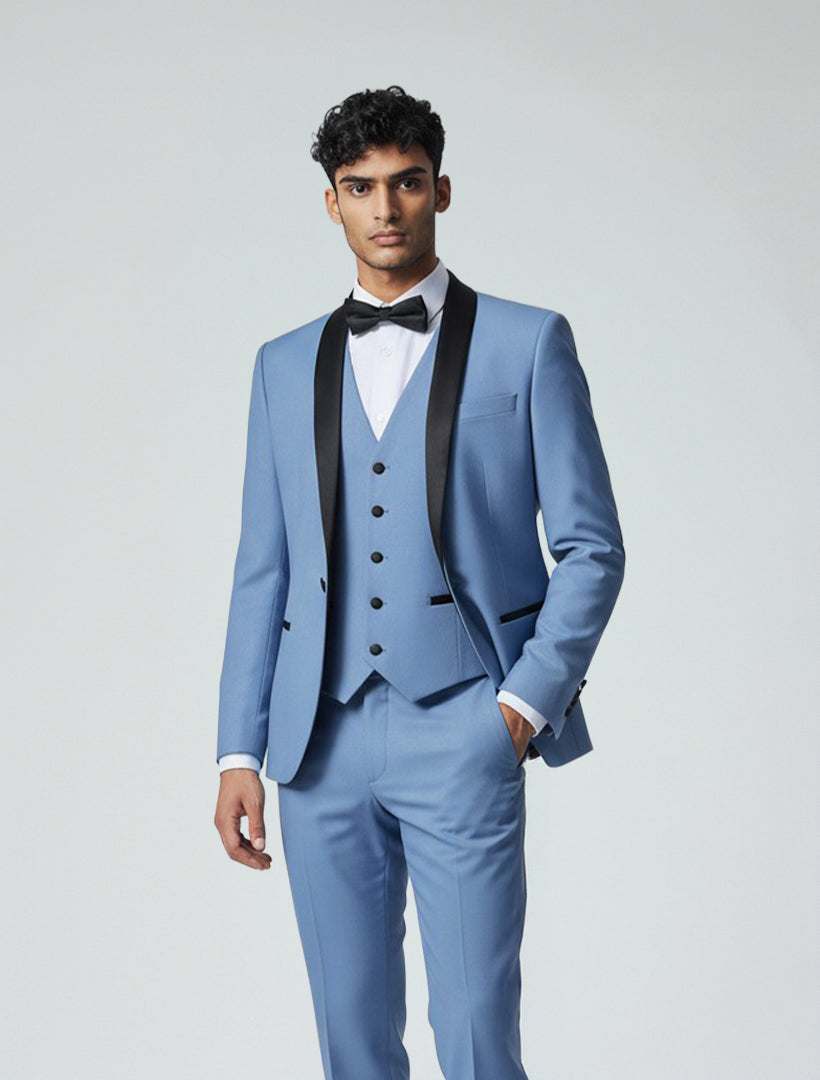 A man stands facing forward wearing the Gino Vitale Men's Slate Blue Shawl Lapel Tailored Fit Tuxedo with matching vest and pants, white shirt, and black bow tie against a plain background.