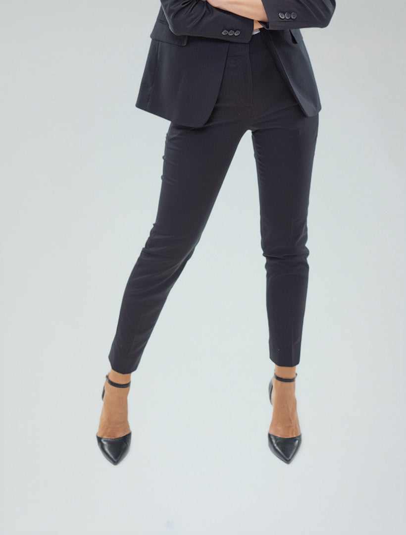 Wearing Couture 1910 Women's Black Suit Separates Pants, a person in professional attire stands confidently with arms crossed and legs apart against a plain light background.