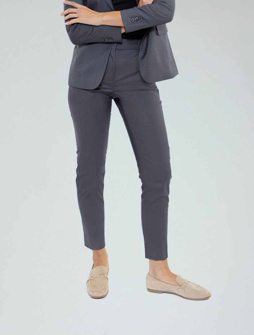 Dressed in Women's Charcoal Grey Suit Separates Pants by Couture 1910, a person in professional attire with beige loafers stands arms crossed against a plain light background.