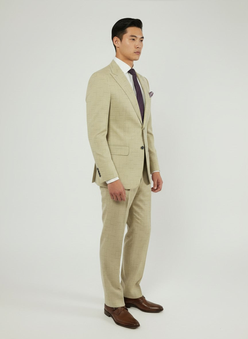 A man stands in a Fubu The Colle FUBU Tan with Navy Fading Windowpane Peak Lapel 2-Piece Suit, paired with a white dress shirt, purple tie, brown shoes, and a pocket square against a plain white background. The slim fit suit features peak lapels and comfortable stretch armholes for modern style and ease of movement.