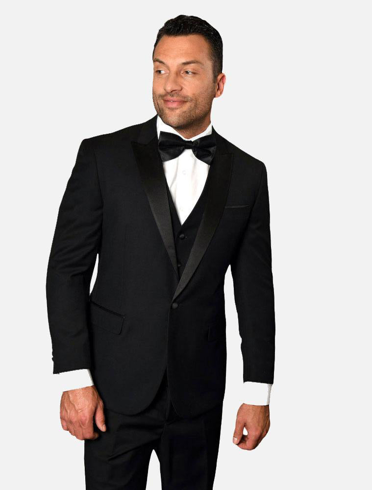 A man in a Statement Men's Black with Black Peak Lapel Vested 100% Wool Tuxedo and a bow tie stands against a plain background, looking to his left.